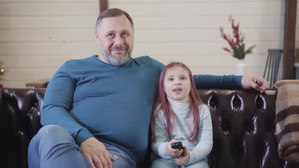 Happy Daughter Watching TV with Father and Talking. Portrait of Joyful Caucasian Girl and Man