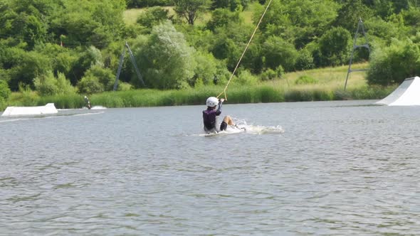 Young Woman Pulled By Towing Rope Gets Up and Rides Wakeboard Near Ramps