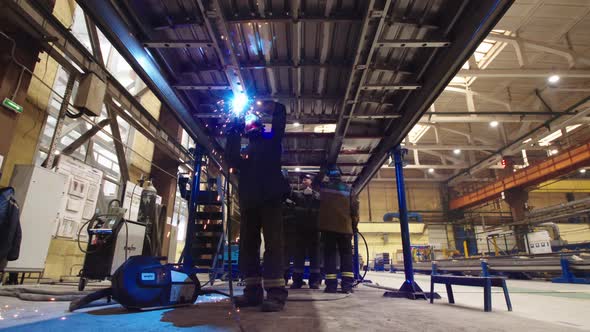 Bottom View of Workers in Protective Uniform and Safety Masks Welding Steel Structures and