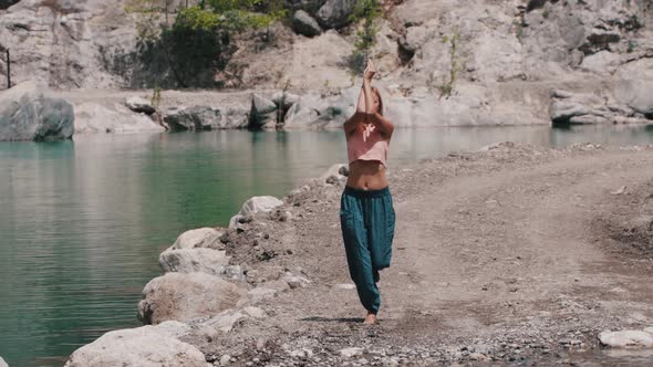 Blonde Woman in Wide Pants Doing Simple Gymnastics By the Lake with Standing on One Leg