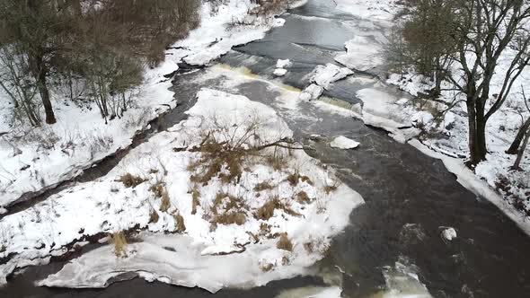 Aerial drone view of a flowing river during winter amongst snowy landscape around. Recorded in Vahik