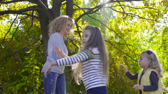 Side View of Young Blonde Woman Staying in the Sunny Park and Blowing Soap Bubbles