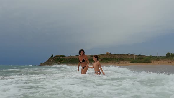 Woman and child bathing in rough sea with big waves at Marinella of Selinunte beach under archaeolog