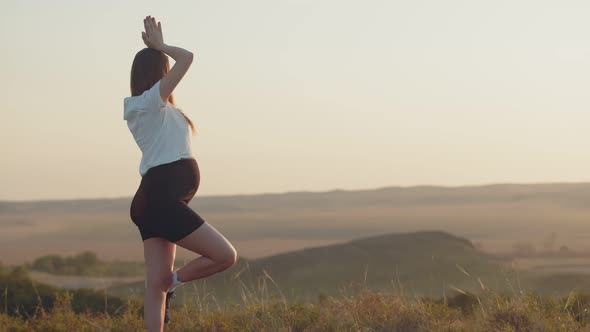 White Pregnant Woman in Sports Clothes is Doing Yoga Outdoor Back View