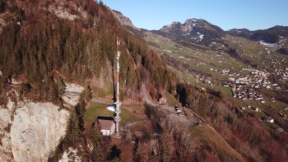 Aerial orbiting shot of radio tower standing on rocky mountain in Swiss Landscape.Sunny day in Amden