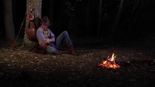 Cowboy Near the Fire in the Forest at Night