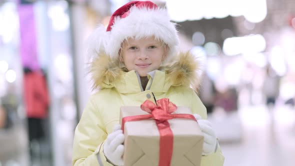 Portrait Winter Little Girl in Santa Hat with Gifts Box in Christmas Shopping Mall Traditional