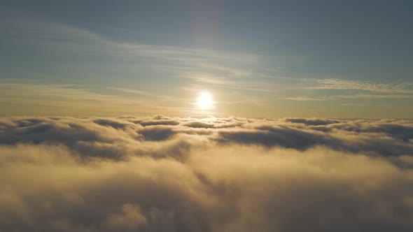 Aerial view of bright yellow sunset over white dense clouds with blue sky overhead.