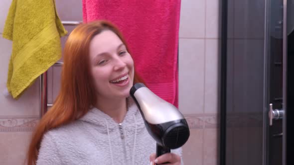 Young Woman Sings with a Hair Dryer in His Hands in Bathroom