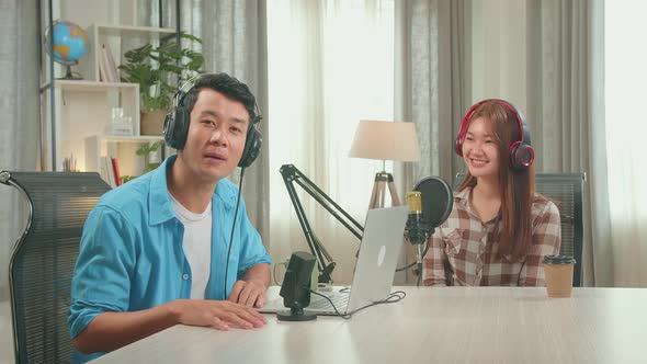 Asian Man Host Record Podcast Wear Headphone Interview Woman Guest, Talking And Looking At Camera