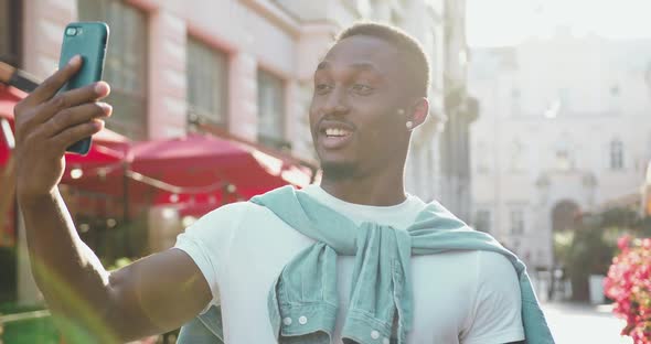 African American in Casual Clothes Has Positive Video call While Standing Near Cozy Street Cafes