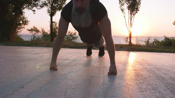 Fit Handsome Middle Aged Man with Long Gray Beard Doing Push Ups on Sports Ground with Sea