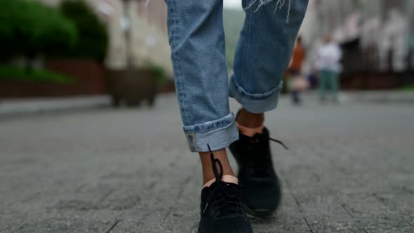 Young Woman is Wearing Ripped Jeans and Black Sneakers and Walking on Street