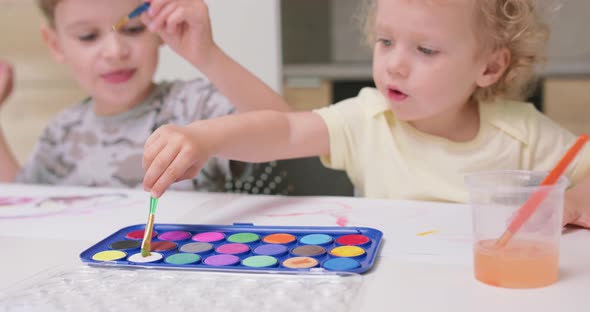 A Boy and a Girl are Sitting at the Table and Trying to Soak Paintbrushes in Watercolors and Talking