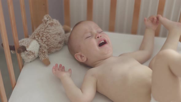 Portrait of Crying Screaming Naked Baby Infant Lying Sitting in Crib Cot Cradle