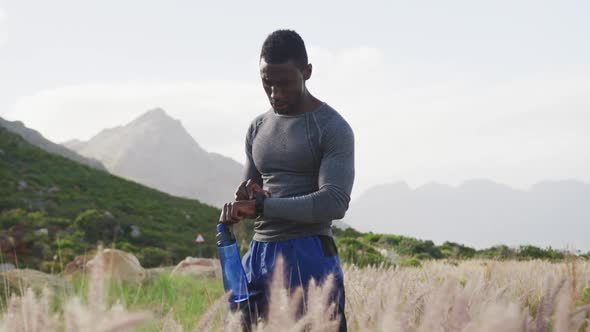 African american man drinking water while exercising in countryside checking his watch