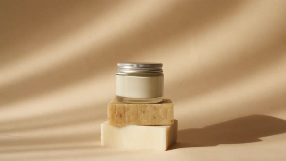 Cream in a Glass Jar on Beige Podiums From Bars of Soap in Sun Light
