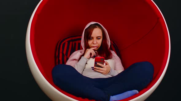 Woman Browsing Smartphone in Egg Armchair