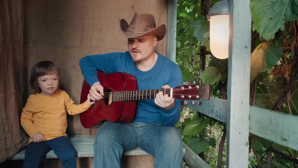 Dad Cowboy Plays an Acoustic Guitar for His Small Child