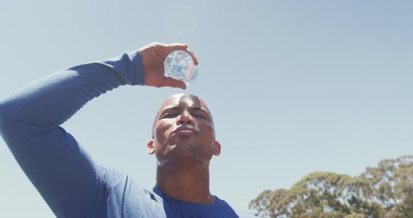 Fit african american man pouring water over shaved head, cooling off after exercising in the sun