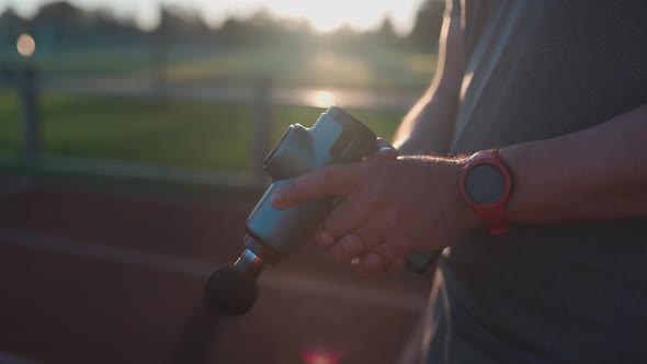 Athletic Male Massages Muscles with Hand Massage Gun Recovering From Stadium Running Workout