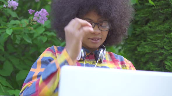 Portrait African American Woman with an Afro Hairstyle Uses a Laptop Sitting on Bench on the Street