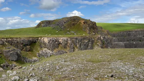 Large hill made from rock with sheep grazing on the grassland and blue sky's