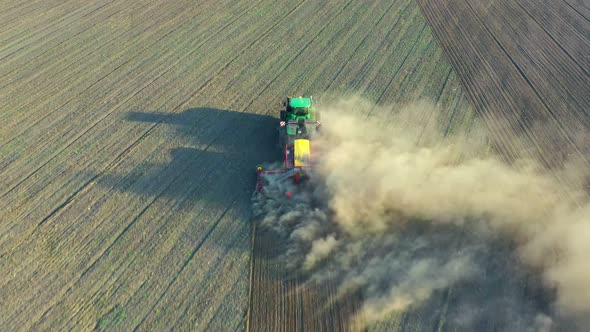 Green tractor cultivating ground and seeding a dry field.