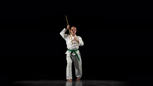 Kendo Fighter on White Kimono Practicing Martial Art with the Bamboo Bokken on Black Background.