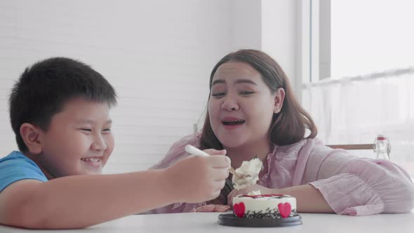 Asian family relationship with son feeding cake with mother in birthday and hug at home.