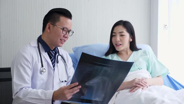 Asian male doctor holding x-ray film, talking to a female patient, and smiling.