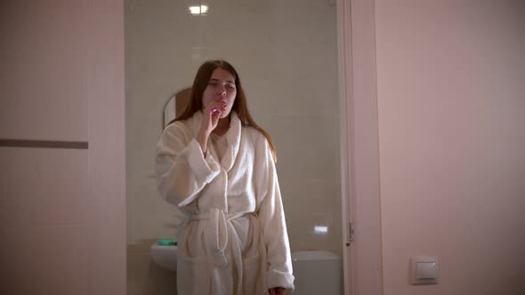 A Young Woman Brushing Her Teeth at the Morning Wearing a Bathrobe
