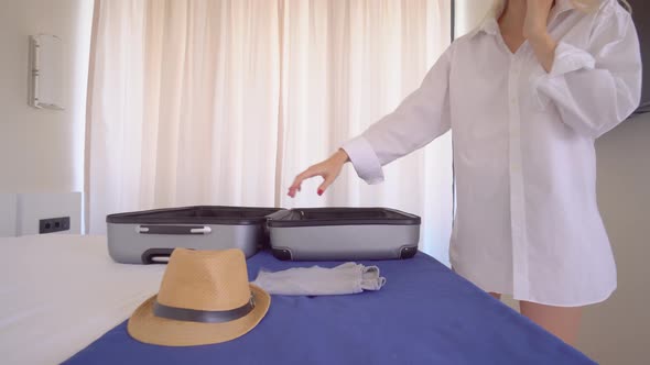 A young beautiful woman in a white shirt puts things out of a suitcase