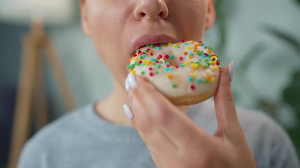 Woman Eating a Sweet Donut in White Glaze with Multicolored Sprinkles