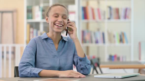 Cheerful African Woman Talking on Smartphone in Library