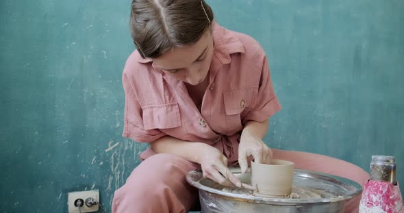 Female Potter Sitting and Makes a Cup on the Pottery Wheel. Woman Making Ceramic Item. Pottery