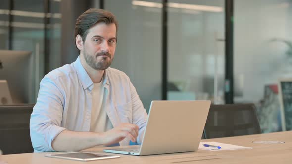 Thumbs Down By Mature Adult Man with Laptop in Office