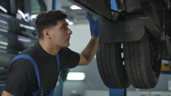 Thoughtful Concentrated Handsome Repairman Checking Auto Parts Under Vehicle