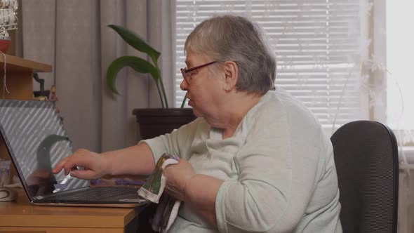 An Elderly Woman Embroiders with Embroidery Scheme on Laptop