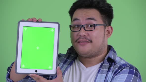 Face of Happy Young Overweight Asian Hipster Man Showing Digital Tablet