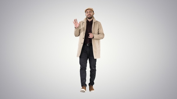 Young man in trench coat makes hi gesture on gradient background