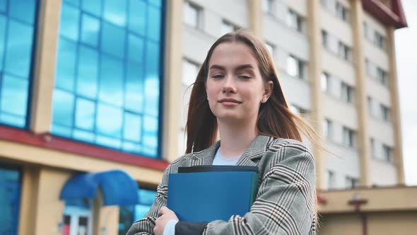 A Young Girl Student Walks Through the City with Folders in Her Hands