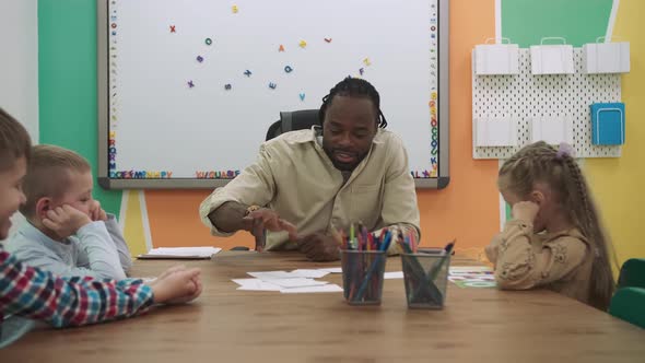 African American Teacher and a Group of Children are Learning Numbers While Sitting at the Table in