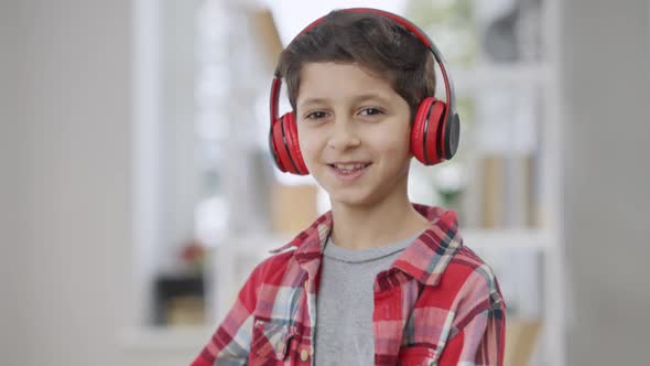 Cheerful Little Boy Listening to Music in Headphones and Dancing Looking at Camera Smiling