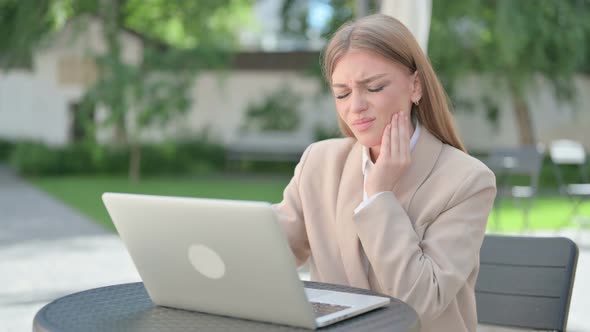 Young Businesswoman with Laptop Having Toothache in Outdoor Cafe