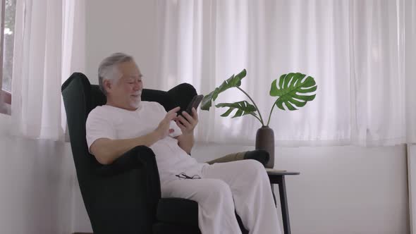 Asian Elderly man use smart phone in living room on a relaxing day.