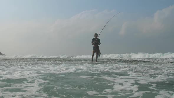 Fisherman Stands in Foaming Ocean Water Under Cloudy Sky