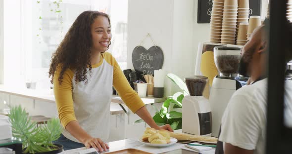 Happy african american male barista taking order from biracial female client at cafe