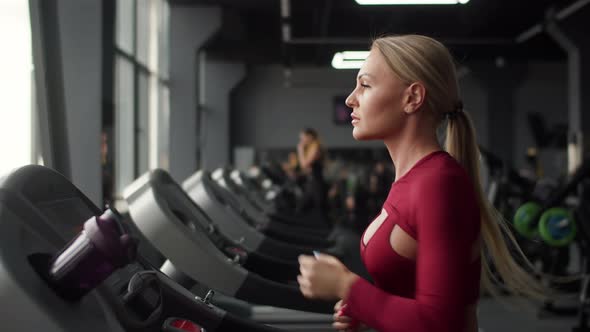 Woman of Athletic Build Runs on Treadmill in Gym and Checks Pulse on Smart Watch Front View