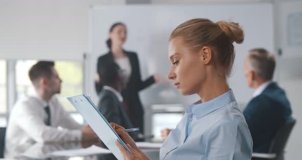 Young Beautiful Businesswoman Writing in Notebook During Seminar